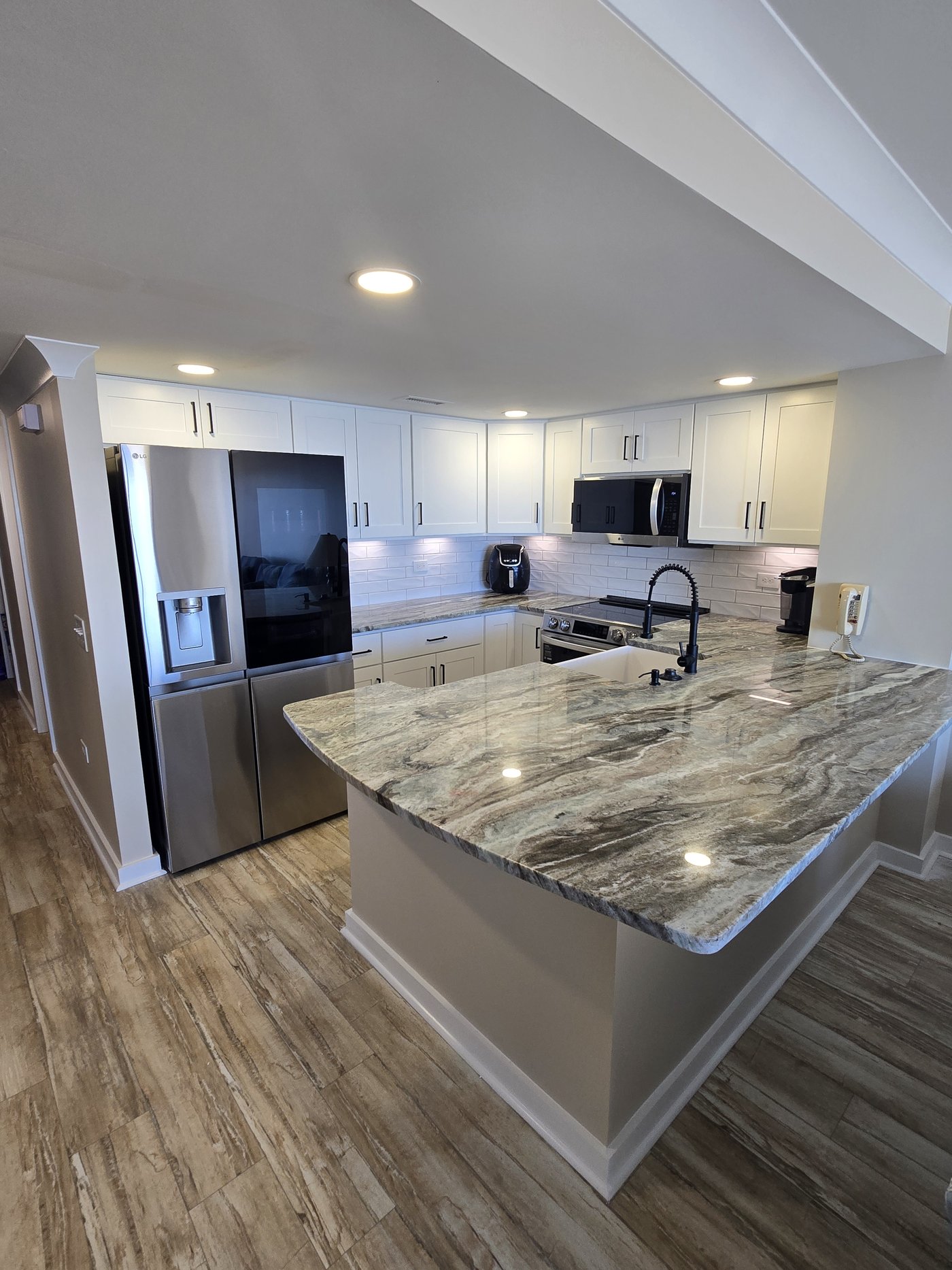 Kitchen after JICON remodel — white shaker cabinets, granite waterfall peninsula and new flooring